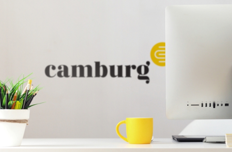 A computer on a desk with the Camburg logo in the background